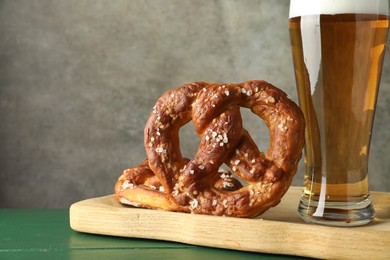 Photo of Tasty pretzels and glass of beer on green wooden table against grey textured background, closeup