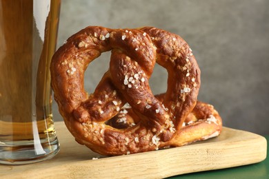 Photo of Tasty pretzels and glass of beer on green wooden table against grey background, closeup