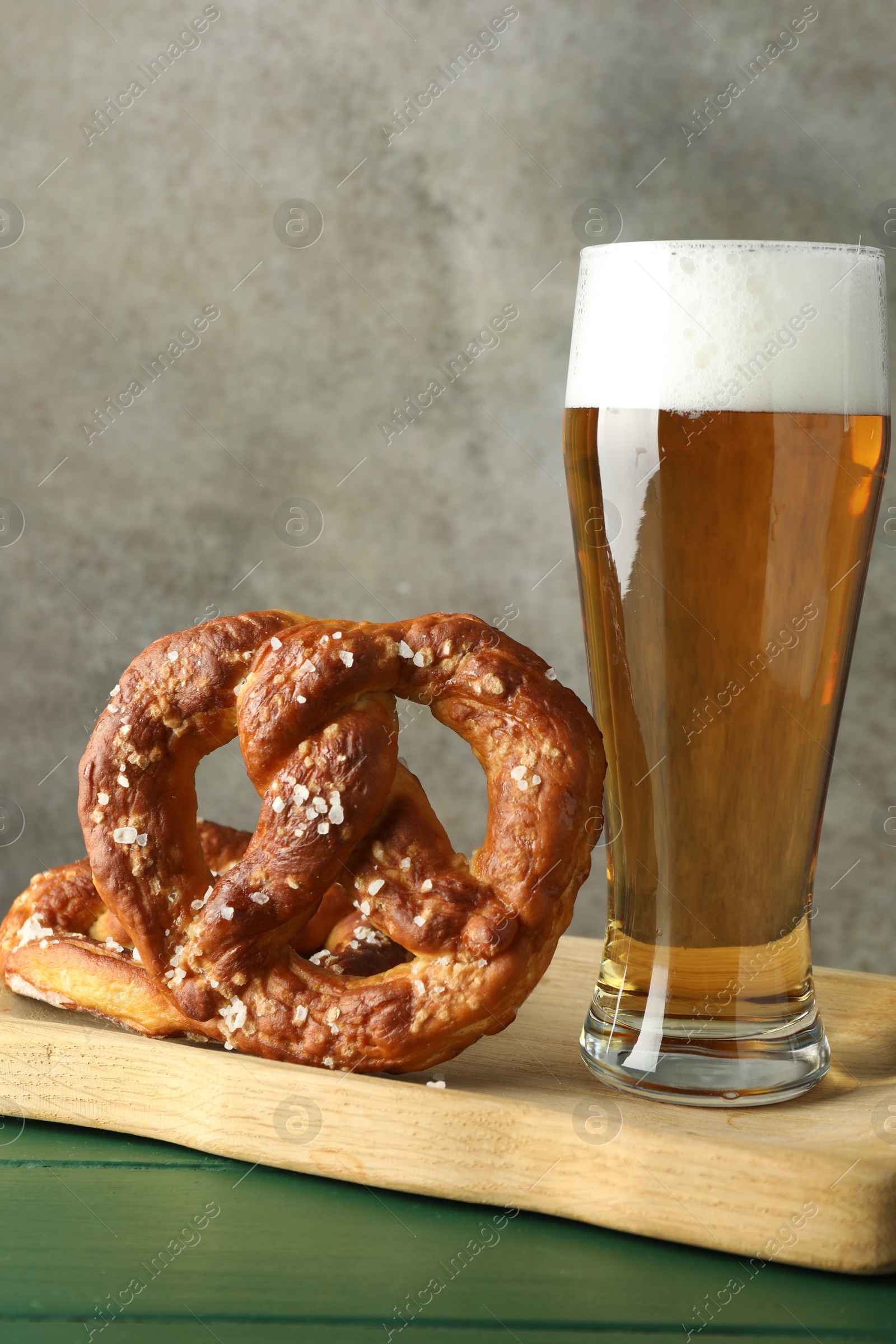 Tasty pretzels and glass of beer on green wooden table against grey textured background, closeup Photo of Tasty pretzels and glass of beer on green wooden table against grey textured background, closeup