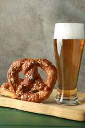 Photo of Tasty pretzels and glass of beer on green wooden table against grey textured background, closeup