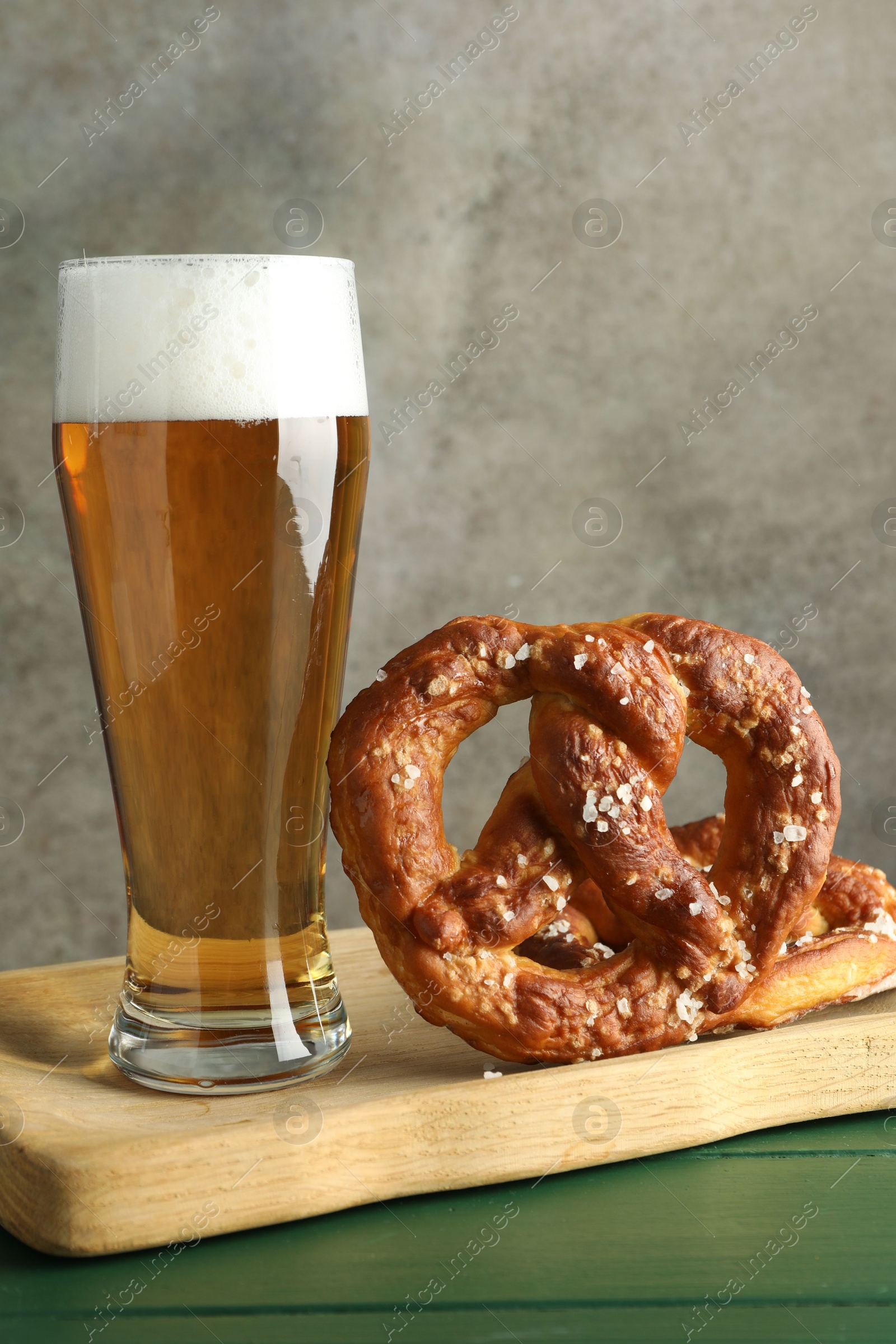 Tasty pretzels and glass of beer on green wooden table against grey textured background, closeup Photo of Tasty pretzels and glass of beer on green wooden table against grey textured background, closeup