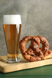 Photo of Tasty pretzels and glass of beer on green wooden table against grey textured background, closeup