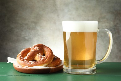 Photo of Tasty pretzels and glass of beer on green wooden table against grey textured background, closeup