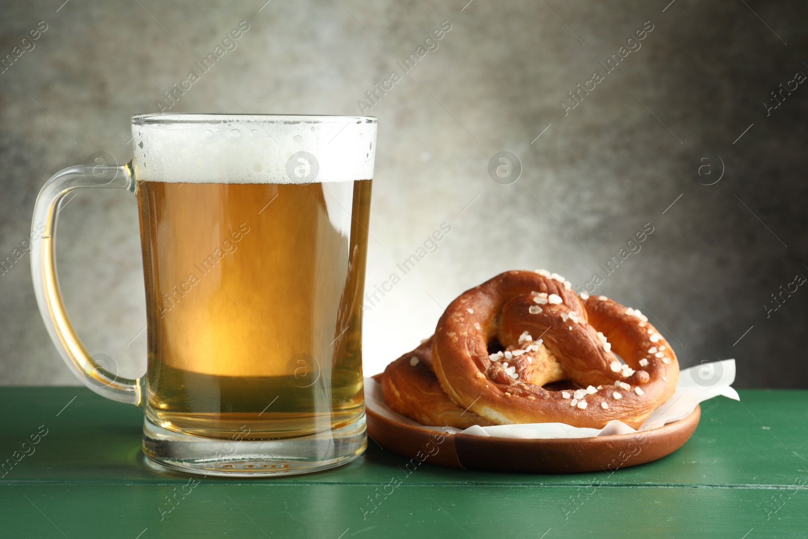 Tasty pretzels and glass of beer on green wooden table against grey textured background, closeup Photo of Tasty pretzels and glass of beer on green wooden table against grey textured background, closeup
