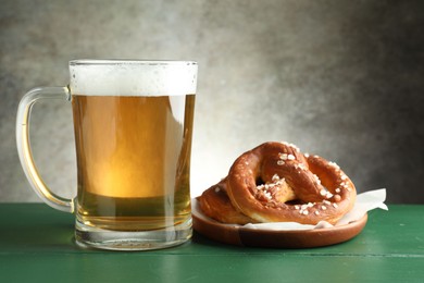 Photo of Tasty pretzels and glass of beer on green wooden table against grey textured background, closeup