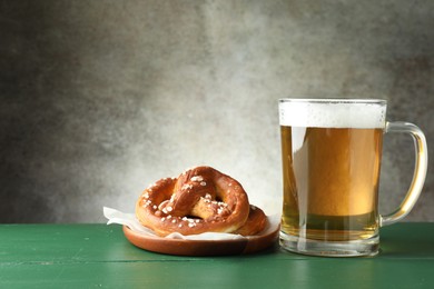 Photo of Tasty pretzels and glass of beer on green wooden table against grey textured background, closeup. Space for text