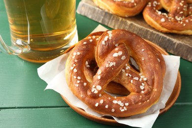 Photo of Tasty pretzels and glass of beer on green wooden table, closeup