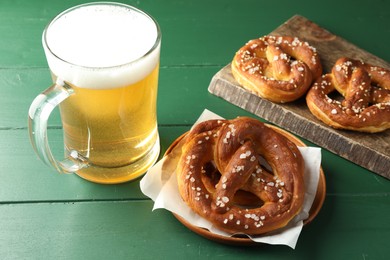 Photo of Tasty pretzels and glass of beer on green wooden table, closeup