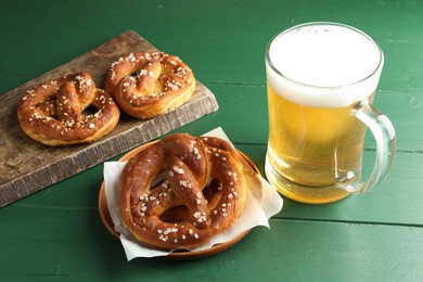 Photo of Tasty pretzels and glass of beer on green wooden table, closeup