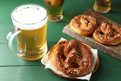 Photo of Tasty pretzels and glasses of beer on green wooden table, closeup