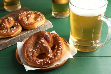 Photo of Tasty pretzels and glasses of beer on green wooden table, closeup