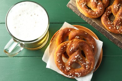 Photo of Tasty pretzels and glass of beer on green wooden table, flat lay