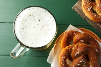 Photo of Tasty pretzels and glass of beer on green wooden table, flat lay