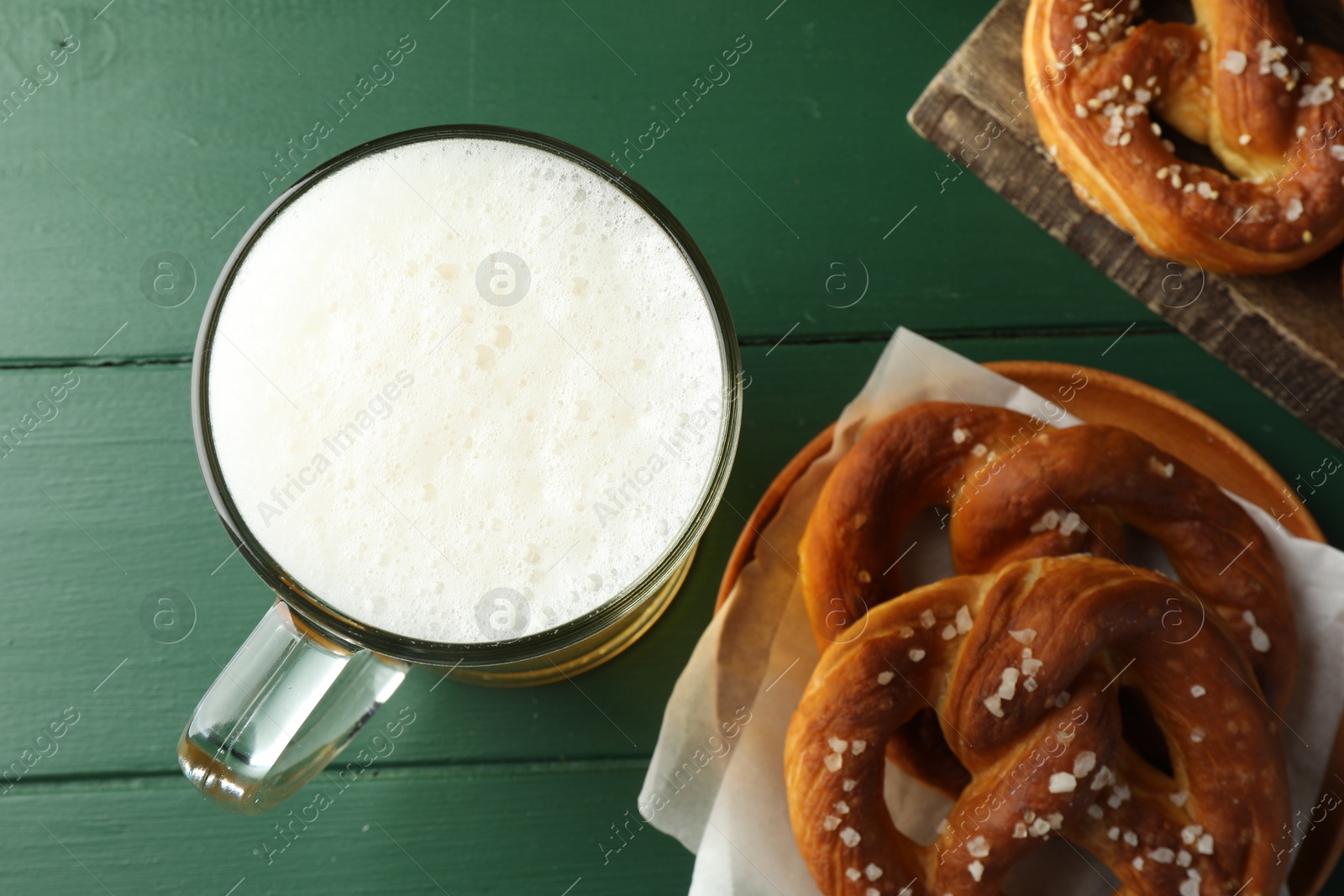 Tasty pretzels and glass of beer on green wooden table, flat lay Photo of Tasty pretzels and glass of beer on green wooden table, flat lay