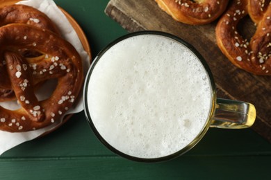 Photo of Tasty pretzels and glass of beer on green wooden table, flat lay