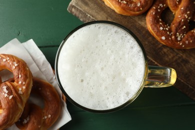 Photo of Tasty pretzels and glass of beer on green wooden table, flat lay