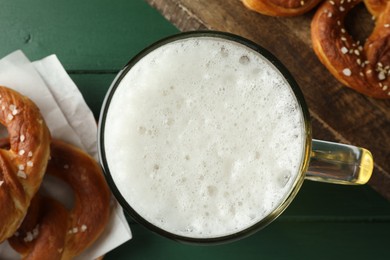 Photo of Tasty pretzels and glass of beer on green wooden table, flat lay
