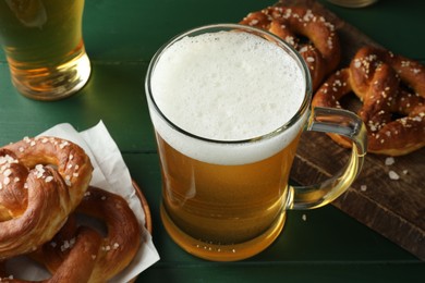 Photo of Tasty pretzels and glasses of beer on green wooden table, closeup