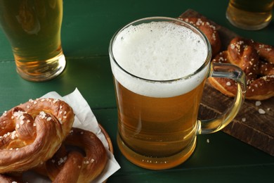 Photo of Tasty pretzels and glasses of beer on green wooden table, closeup