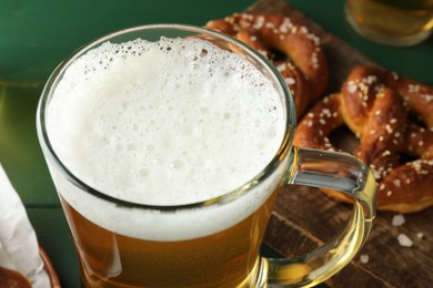 Photo of Glass of beer and tasty pretzels on green table, selective focus
