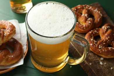 Photo of Tasty pretzels and glass of beer on green wooden table, closeup