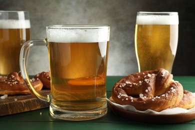 Photo of Tasty pretzels and glasses of beer on green wooden table against grey background, closeup