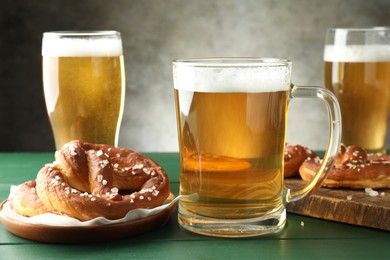 Photo of Tasty pretzels and glasses of beer on green wooden table against grey background, closeup