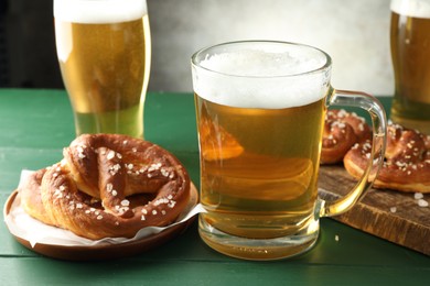 Photo of Tasty pretzels and glasses of beer on green wooden table against grey background, closeup