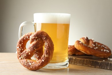 Photo of Tasty pretzels and glass of beer on wooden table against grey background, closeup