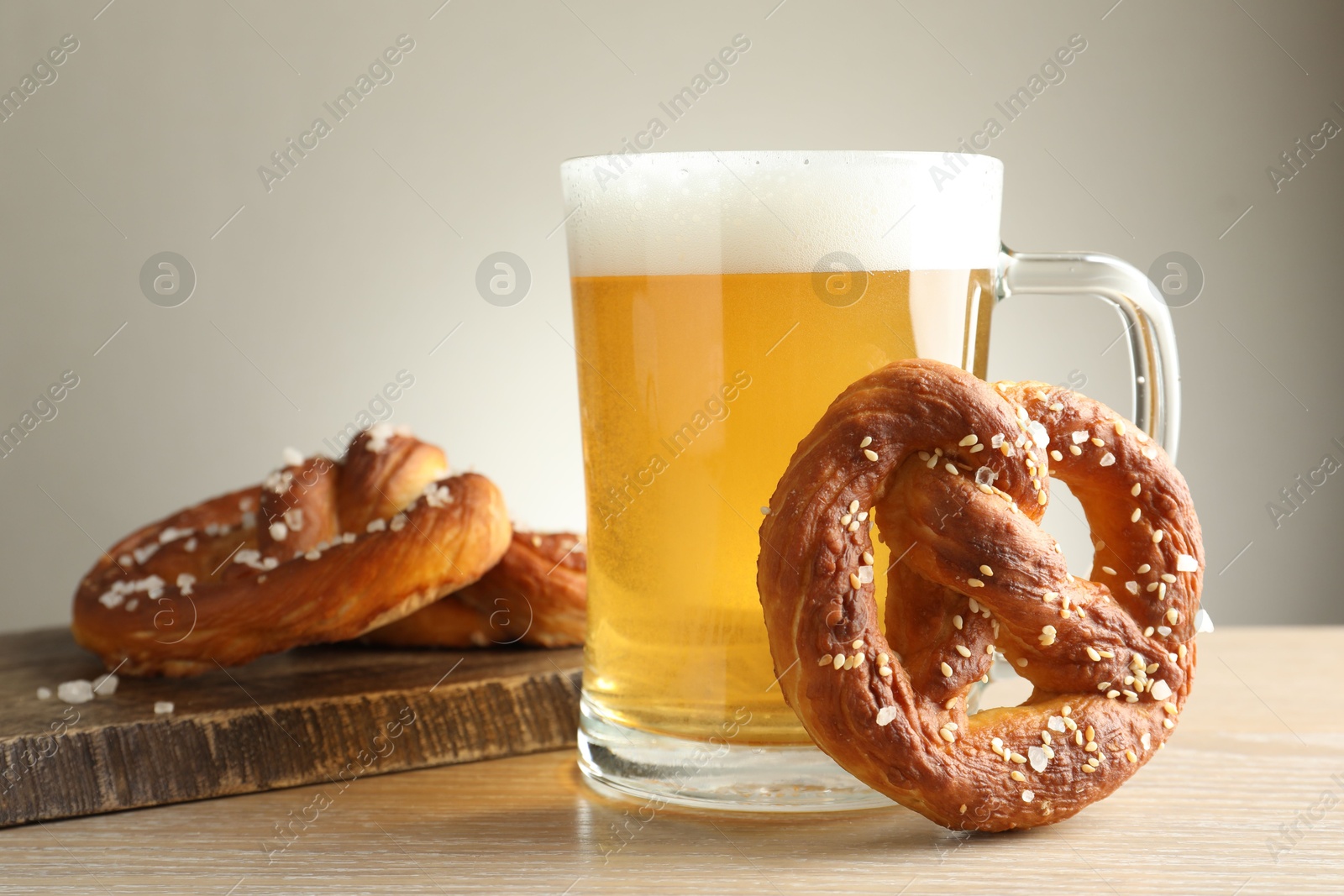 Tasty pretzels and glass of beer on wooden table against grey background, closeup Photo of Tasty pretzels and glass of beer on wooden table against grey background, closeup