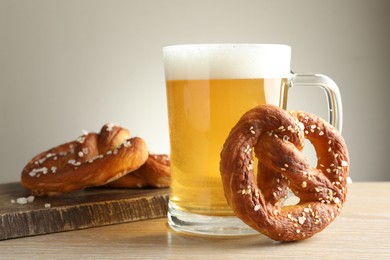 Photo of Tasty pretzels and glass of beer on wooden table against grey background, closeup