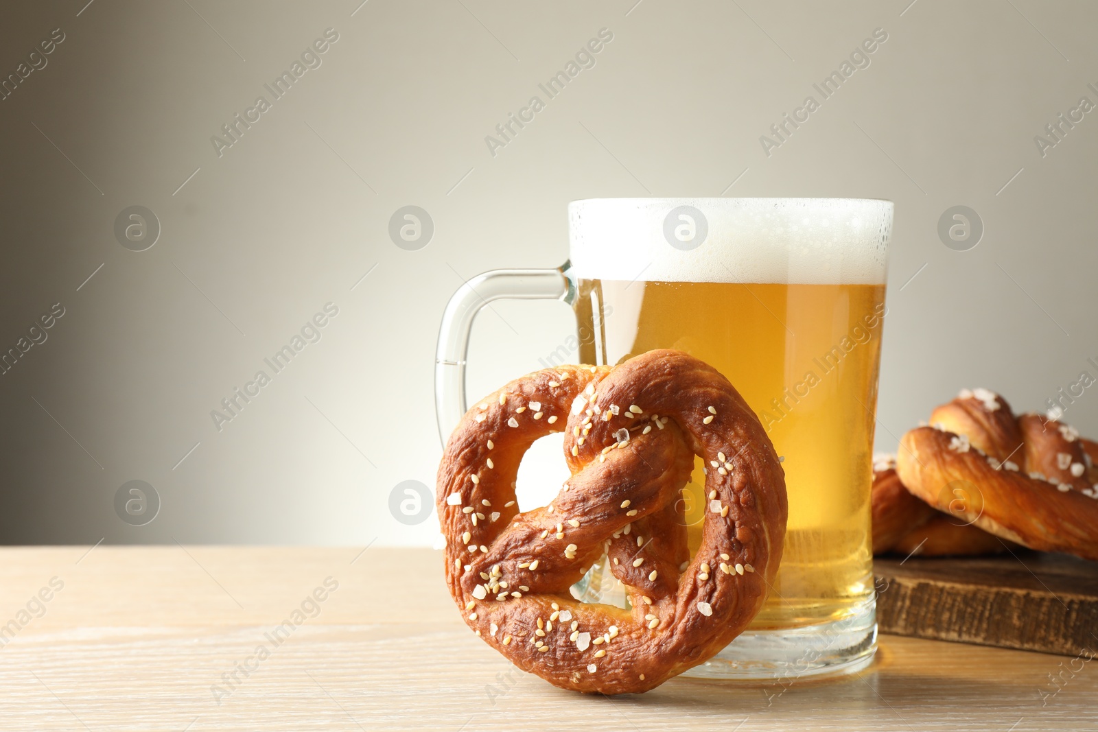 Photo of Tasty pretzels and glass of beer on wooden table against grey background, closeup. Space for text