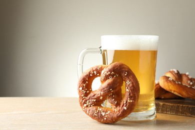 Photo of Tasty pretzels and glass of beer on wooden table against grey background, closeup. Space for text