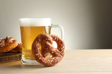 Photo of Tasty pretzels and glass of beer on wooden table against grey background, closeup. Space for text