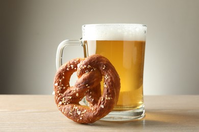 Photo of Tasty pretzel and glass of beer on wooden table against grey background, closeup
