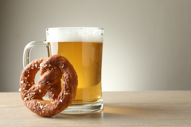 Photo of Tasty pretzel and glass of beer on wooden table against grey background, closeup. Space for text