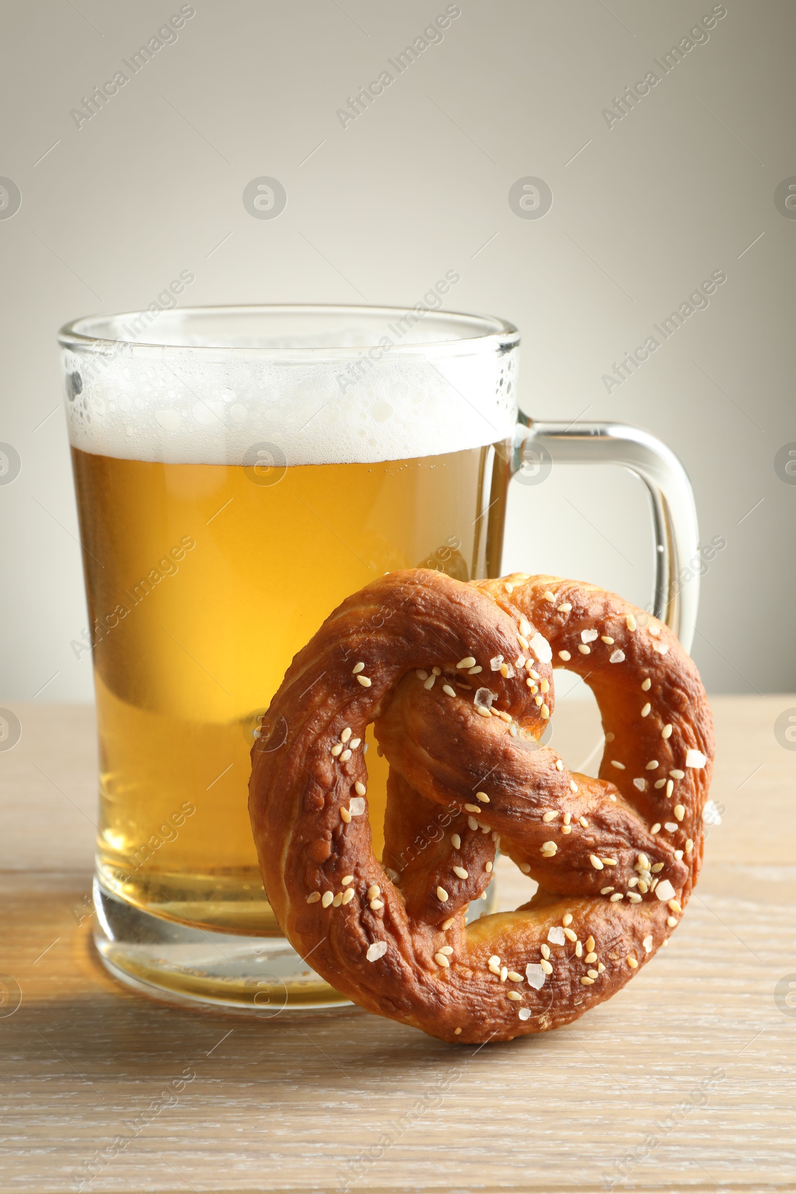Tasty pretzel and glass of beer on wooden table against grey background, closeup Photo of Tasty pretzel and glass of beer on wooden table against grey background, closeup