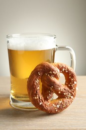 Photo of Tasty pretzel and glass of beer on wooden table against grey background, closeup