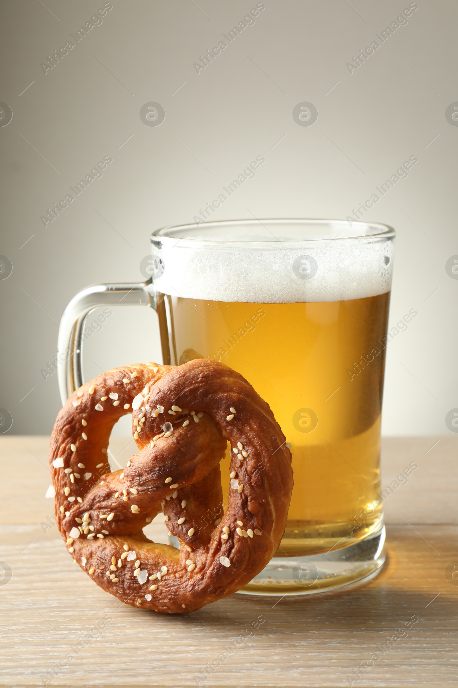 Tasty pretzel and glass of beer on wooden table against grey background, closeup Photo of Tasty pretzel and glass of beer on wooden table against grey background, closeup