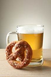 Photo of Tasty pretzel and glass of beer on wooden table against grey background, closeup