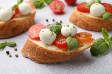 Photo of Tasty sandwiches with mozzarella cheese balls, tomato and basil on light grey table, closeup