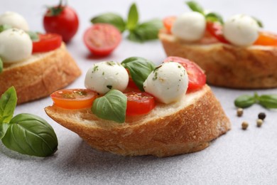 Photo of Tasty sandwiches with mozzarella cheese balls, tomato and basil on light grey table, closeup