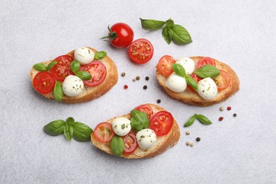 Photo of Tasty sandwiches with mozzarella cheese balls, tomato and basil on light grey table, flat lay