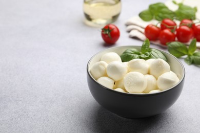 Photo of Tasty mozzarella cheese balls, tomatoes and basil on light grey table, closeup. Space for text