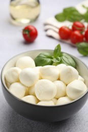 Photo of Tasty mozzarella cheese balls, tomatoes and basil on light grey table, closeup