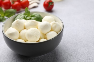 Photo of Tasty mozzarella cheese balls, tomatoes and basil on light grey table, closeup. Space for text