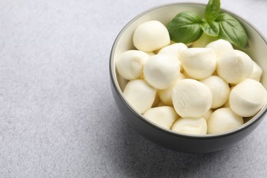 Photo of Tasty mozzarella cheese balls and basil on light grey table, closeup. Space for text