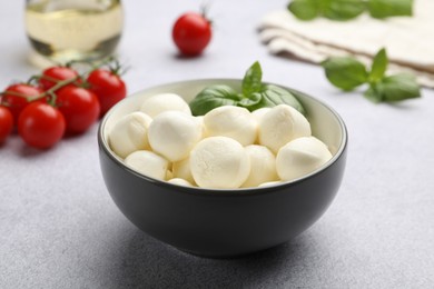 Photo of Tasty mozzarella cheese balls, tomatoes and basil on light grey table, closeup