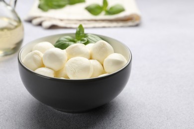 Photo of Tasty mozzarella cheese balls and basil on light grey table, closeup. Space for text
