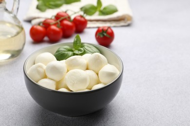 Photo of Tasty mozzarella cheese balls, tomatoes and basil on light grey table, closeup. Space for text